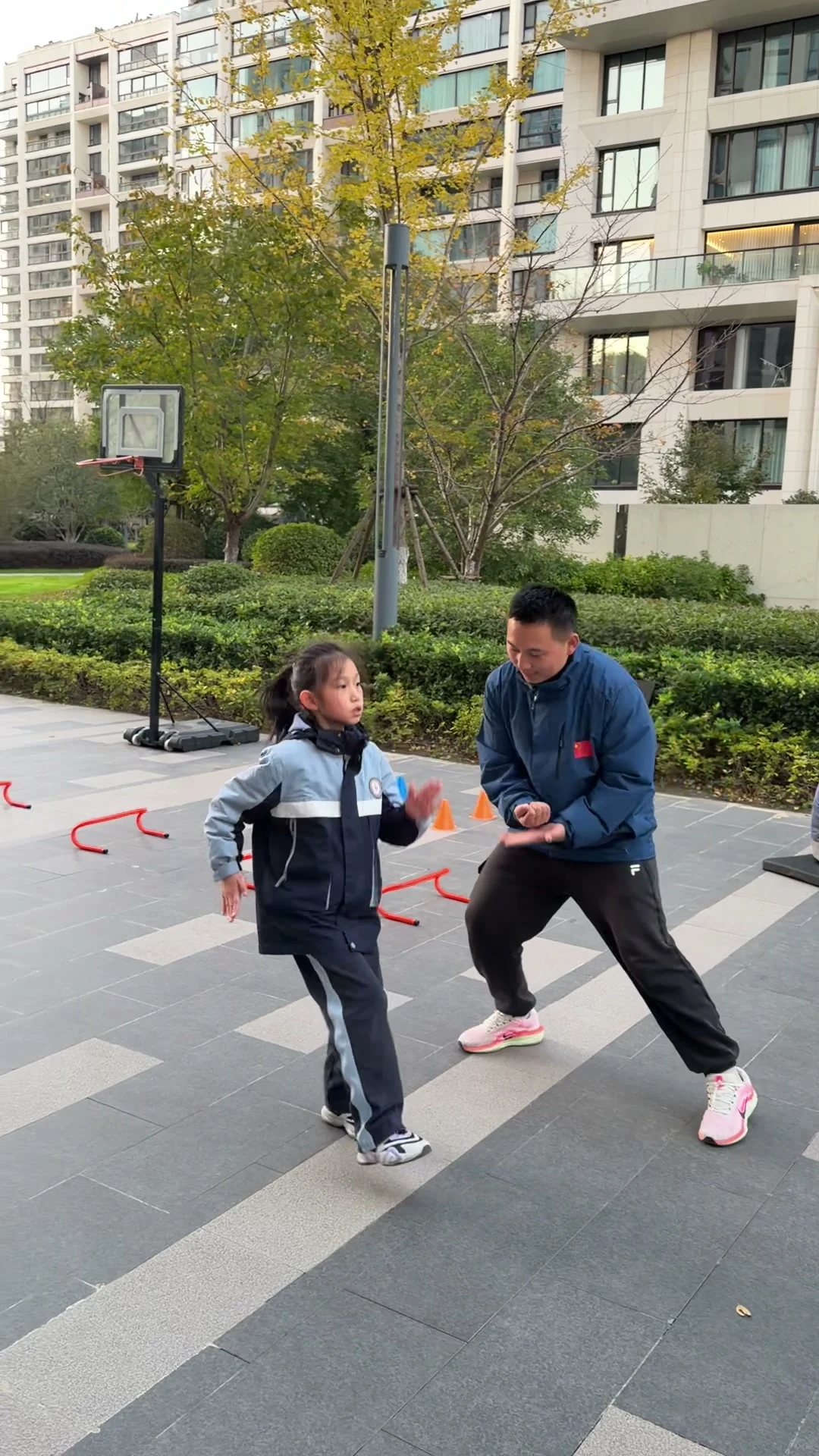 成人在儿童旁示范手臂动作,周围布置低栏与标志桶